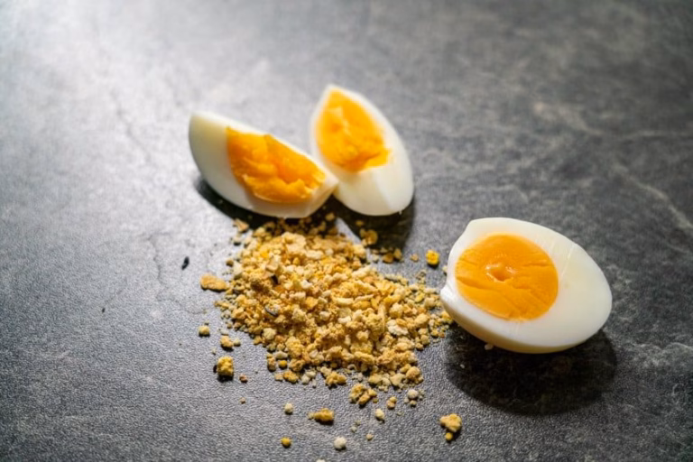 Eifutter für Wellensittiche – Anwendung, Inhaltsstoffe & Dosierung erklärt 20 Eifutter für Wellensittiche – Pulver mit zwei halben Eiern auf grauer Fläche